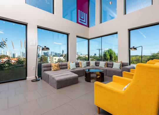 A bright yellow chair is in the foreground of a spacious room with a view of the city.