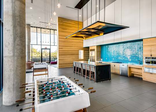 A foosball table is in the middle of a room with a kitchen area.