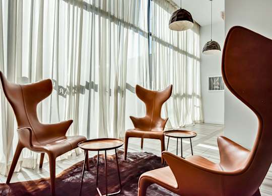 A room with white walls and a large window with curtains, and a set of chairs and tables.