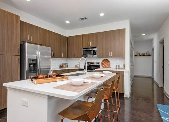 A modern kitchen with a white island and wooden chairs.