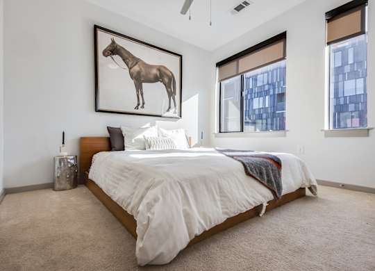 A bedroom with a bed, pillows, a blanket, a ceiling fan, and a framed picture of a horse on the wall.