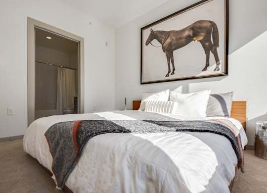 A bedroom with a bed, pillows, a blanket, and a painting of a horse on the wall.