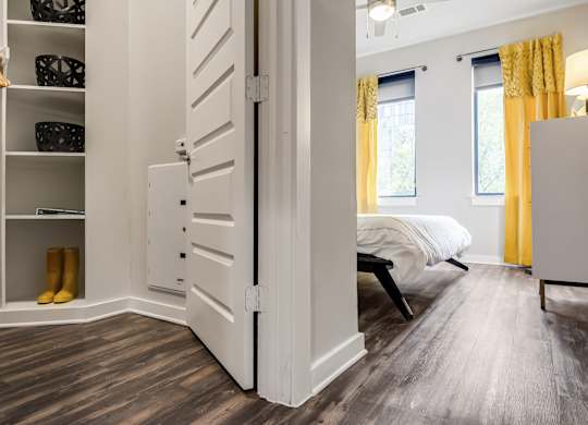 A white closet with a white door is open to a bedroom with a bed and a window.