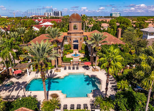 Aerial view of Mediterranean-style clubhouse with pool, palm trees, and courtyard fountain