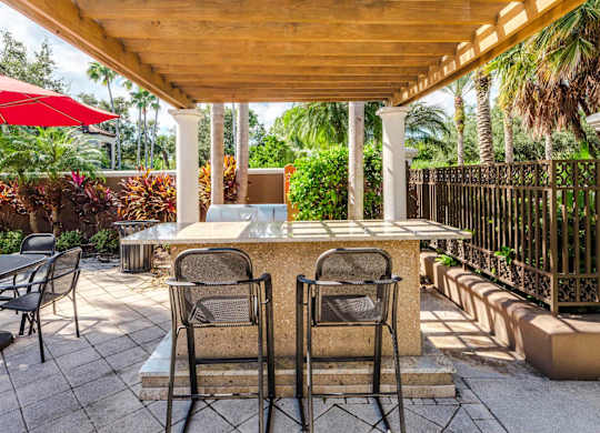 Outdoor grilling station under a pergola with bar seating and tropical landscaping