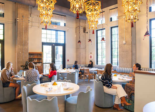A group of people are sitting at tables in a large room with yellow chandeliers.