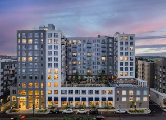 A large, modern apartment building with multiple balconies and a parking lot in front.