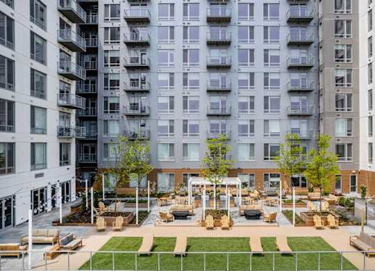 A large grassy area with benches and a pavilion is surrounded by apartment buildings.