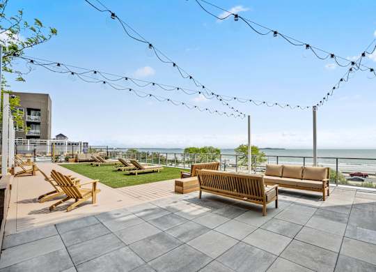 A patio with wooden furniture and string lights overlooking the ocean.