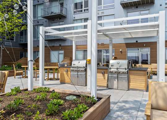 A patio with a grill and chairs is surrounded by a building.