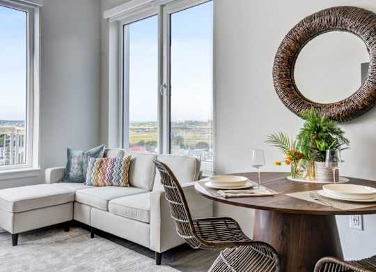 A dining room with a round table and chairs, a bench, and a view of the city through the windows.