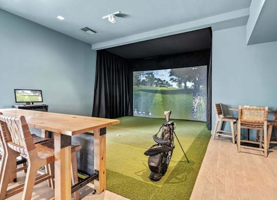 A room with a golf simulator and a table with chairs.