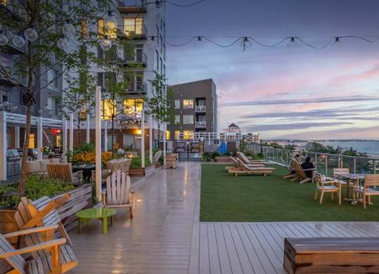 A rooftop patio with wooden furniture and string lights.