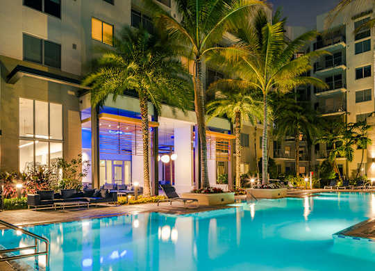 Resort style swimming pool surrounded by palm trees and lounge chairs at Pearl Flagler Village.