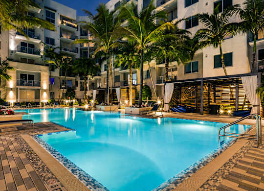 A large swimming pool surrounded by palm trees and a building in the background.