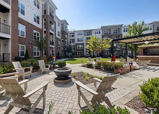 A patio with chairs and a fire pit in front of apartment buildings.