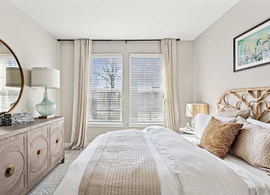 A bedroom with a large bed, a dresser with a mirror, and a window with blinds.