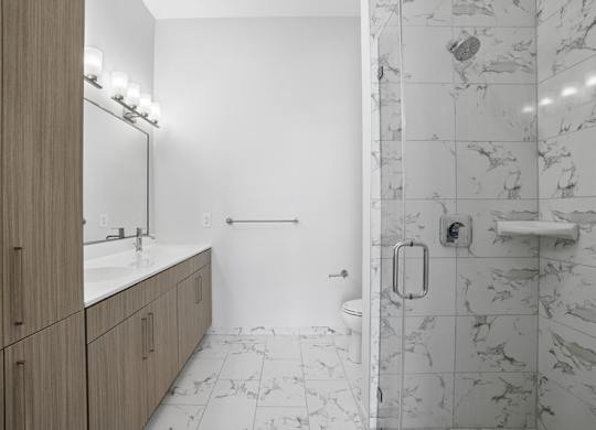 Penthouse bathroom with a marble-look tiled step-in shower, a long quartz vanity and a full-height linen cabinet.