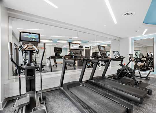 A gym with treadmills, elliptical machines, and a television screen.