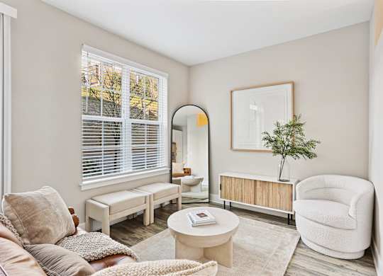 A living room with a white chair, a white sofa, a white coffee table, a white rug, a white wall, a white window with white blinds, a white floor, a white ceiling, a white picture frame, a white