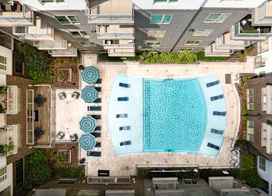 A swimming pool surrounded by a patio with chairs and umbrellas.
