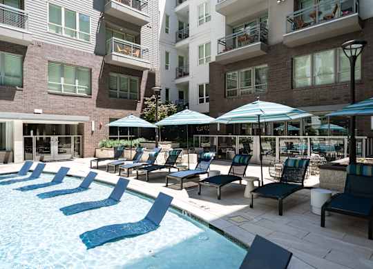 A pool area with chairs and umbrellas in front of apartment buildings.