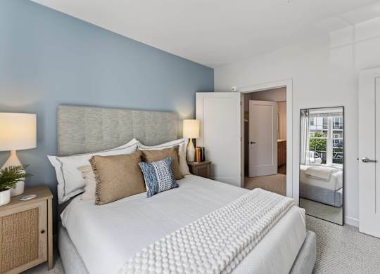 Second view of a bedroom with a blue accent wall, upholstered bed, mirror, and doorway.