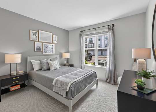 Apartment bedroom with a queen bed, bedside tables, lamps, and a large window.