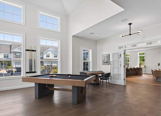 Pool table centered in a bright game room with tall windows and lounge seating.