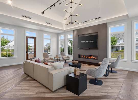 Clubhouse seating area with a sectional sofa, armchairs, fireplace, and tall windows.