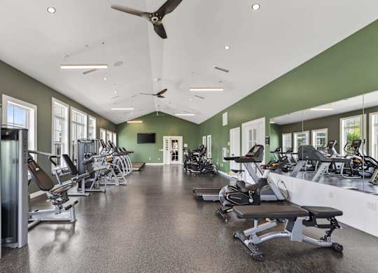 Fitness studio with strength machines, benches, free weights, mirrors, and ceiling fans.