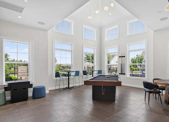 Game room with a pool table, lounge chairs, tall windows, and pendant lighting.