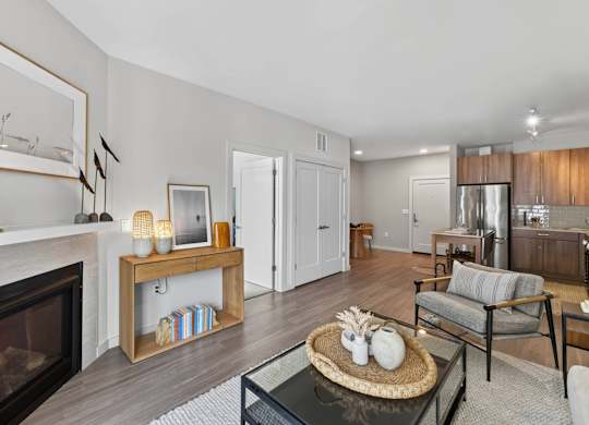 Apartment living room with a gas fireplace, console table, armchair, and open kitchen beyond.