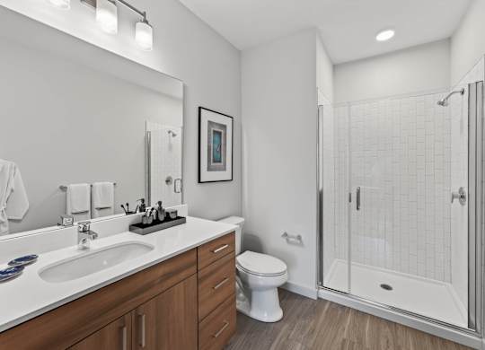 Apartment bathroom with a double vanity, toilet, and glass-enclosed shower.