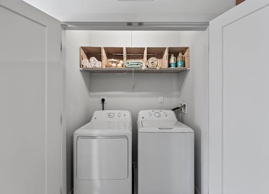 Laundry closet with a full-size washer and dryer beneath open storage cubbies.