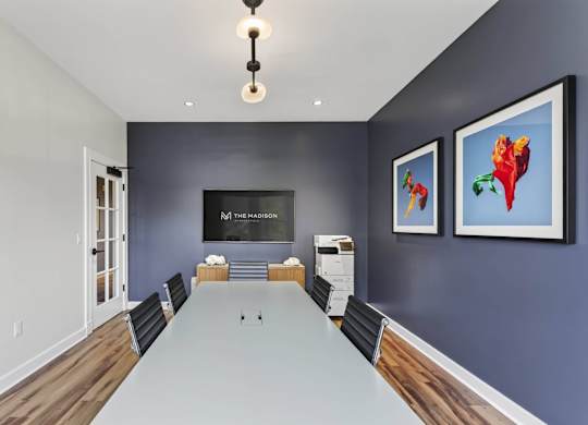 Meeting room with a long white table, black chairs, artwork, and a wall screen.