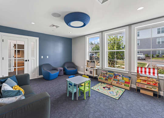 Indoor playroom with a sofa, small tables, book displays, and colorful toys.