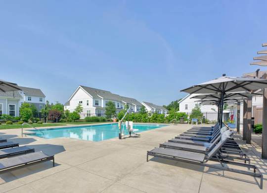 Pool deck with rows of lounge chairs, umbrellas, and a view toward the clubhouse.