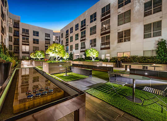 Courtyard game lounge with illuminated shuffleboard table, greenery, and intimate seating under the night sky