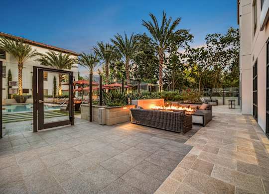 Fire pit lounge with woven seating, glowing flames, and palm-lined views creating a resort-style retreat