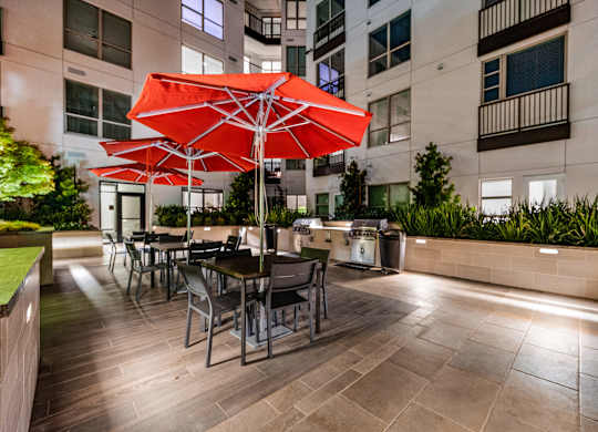 Outdoor dining area with grilling stations, red umbrellas, and modern seating for lively evenings with friends