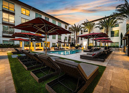 Poolside retreat with red umbrellas, plush loungers, and a glowing sunset backdrop