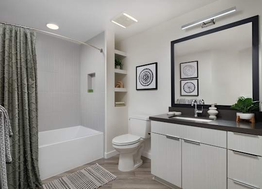 Bathroom with a tub behind a patterned curtain, a tiled niche, built-in shelving and a dark quartz vanity opposite the tub.