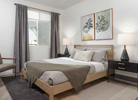 Bedroom with an oak bed frame, olive bedding, framed botanical prints and an armchair beside the window and a grey rug.