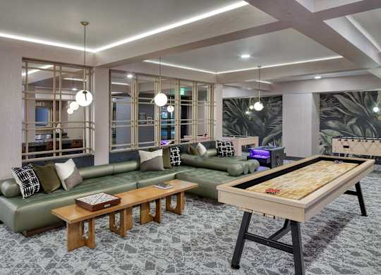 Game lounge with a green leather sectional, timber bench, shuffleboard table and brass lattice screens dividing the room.