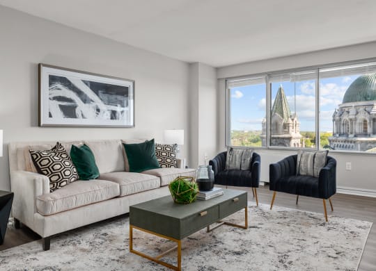 a living room with a beige couch and two black and white chairs and a large window