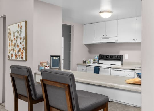 a kitchen with white cabinets and a counter with two chairs