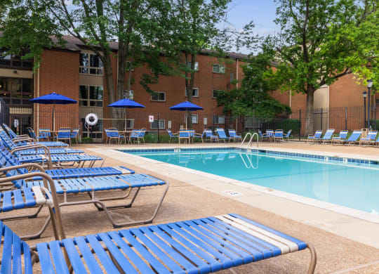 a swimming pool with chaise lounge chairs and umbrellas in front of a brick building