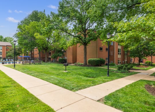 a grassy area with trees and a walkway in front of a brick building