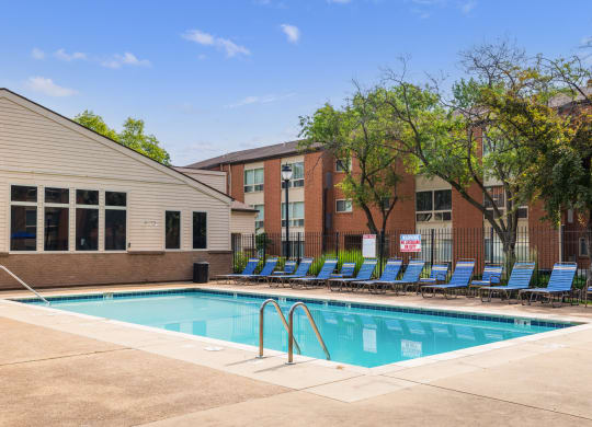 a swimming pool with blue chaise lounge chairs and a brick building in the background